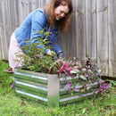 Women kneeling next to square, silver raised garden bed outside tending to plants