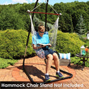 Man with sunglasses reading while sitting in hammock seat swing with wooden spreader hanging from hammock chair stand on an outdoor brick patio