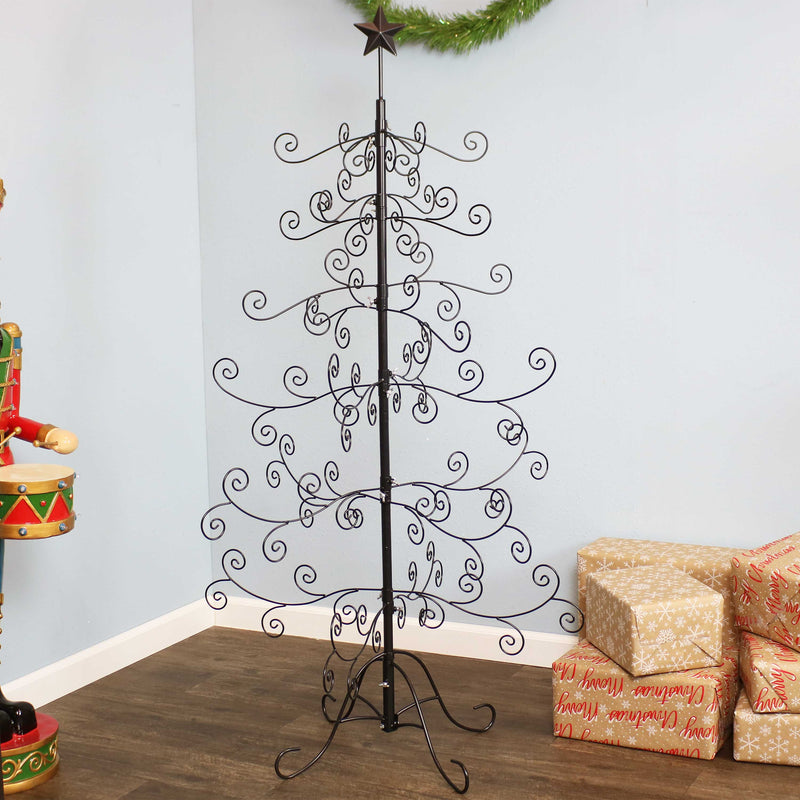A metal Christmas ornament tree is decorated with red, green, and gold ornaments and displayed in a living room.
