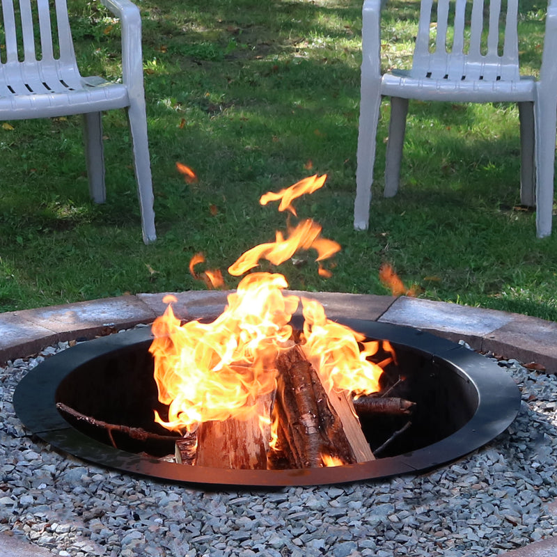 A wood-burning fire pit liner is surrounded by bricks to create an above-ground fire pit in the grass.
