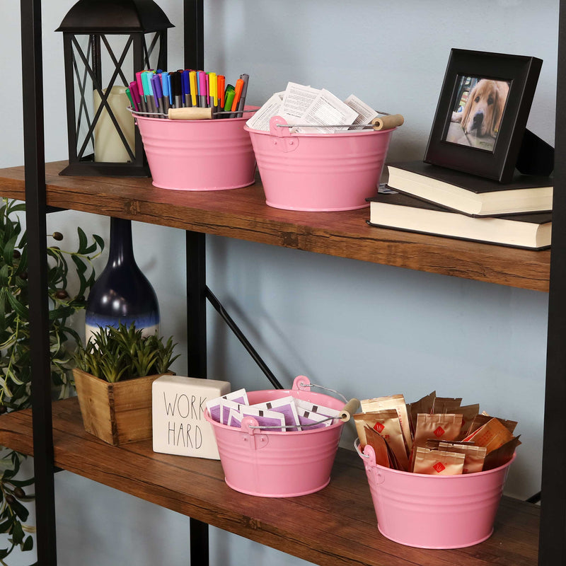 
Four pink galvanized steel buckets with handle filled with various items placed bookshelf containing books and pictures.