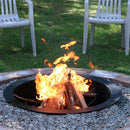 A DIY in-ground fire pit liner surrounded by rocks is used to create a campfire in the backyard.
