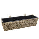 Long, light brown wicker planter basket with plants planted in the liner hooked on wooden fencing.