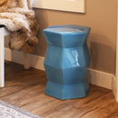 Blue geometric ceramic garden stool being used as side table in a living room near a chair with a fuzzy blanket
