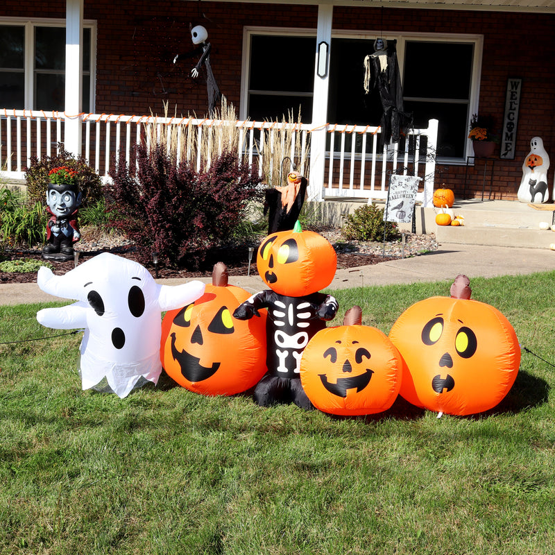 Pumpkin patch inflatable containing a ghost, three pumpkins, and one pumpkin skeleton staked in a front lawn decored for Halloween