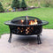 An outdoor large fire pit with a diamond crossweave design burns firewood in the backyard with a spark screen covering the flame.
