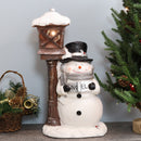 Jack the frosty snowman figurine  with antique street lamp sitting on indoor entryway table next to a tabletop Christmas tree