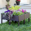 Four self-water raised garden beds placed on a front lawn full of lush flowers and plants.