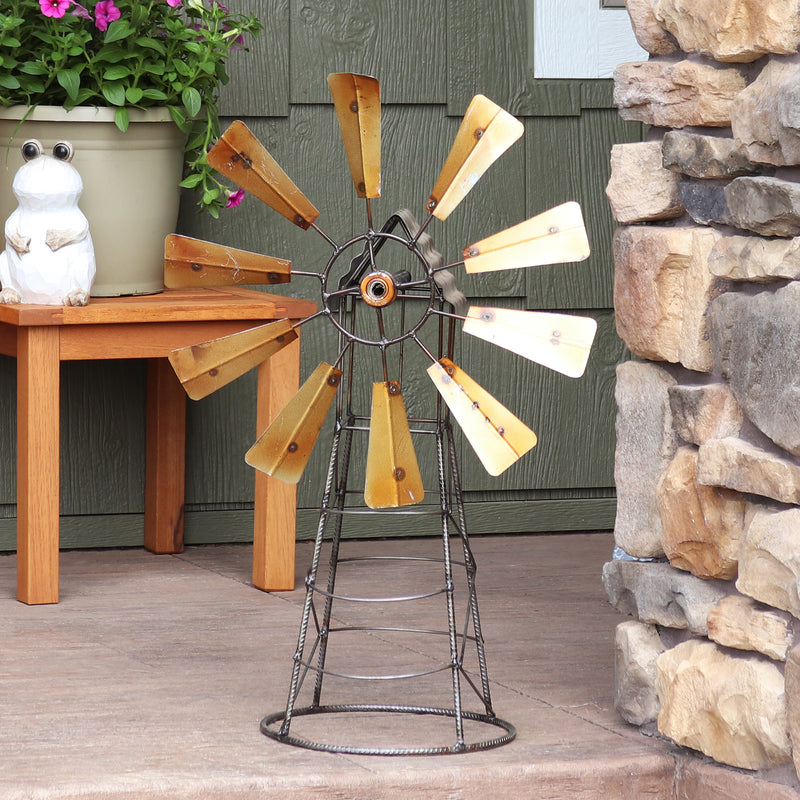 Metal windmill with golden blades sitting on a porch.