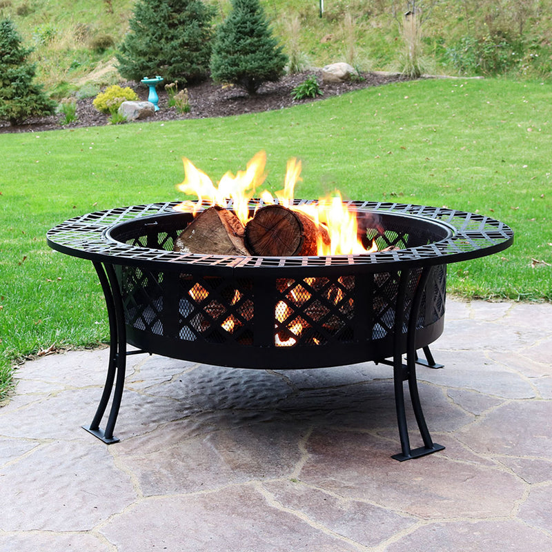 An outdoor steel fire pit with an open flame on a stone patio in the backyard.
