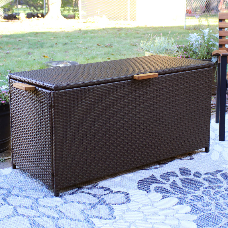 Brown resin rattan deck box with acacia wood handles outdoors on a floral rug
