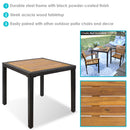 Square faux wicker patio table with steel frame and acacia wood surface sitting on outdoor patio with floral rug in between two patio chairs