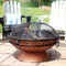 Copper-colored burning fire pit with spark screen resting on the rim.