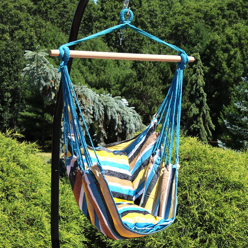 Stripped hammock chair hanging from a stand with trees in the background.