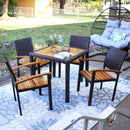 An outdoor dining set sits on a floral outdoor rug on a patio with a plant and book placed on the table.
