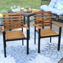 Two acacia wood patio chairs sitting on outdoor patio with gray rug, in front of square patio table