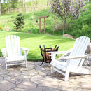 Two white Adirondack chairs with a log holder between them on a stone patio.