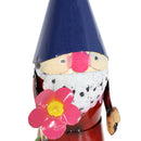 Metal garden gnome with a rosy pink nose, white beard in a red shirt holding an pink flower.