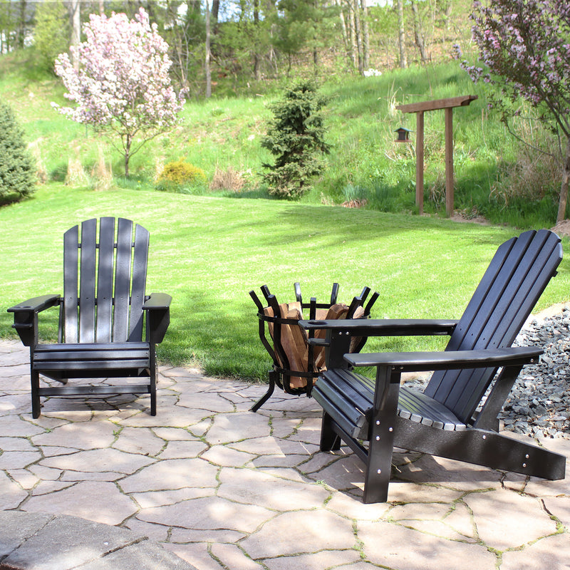 Two black Adirondack chairs sit on a stone patio, in between them in a fluted log holder full of wood.